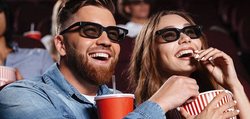 Una coppia giovane di ragazzi che guardano un film al cinema con occhiali 3D, una bibita e dei pop-corn